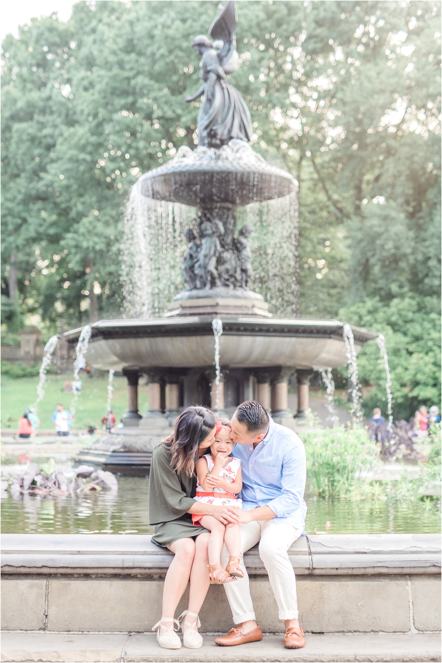 family sitting by fountain kissing baby's cheeks